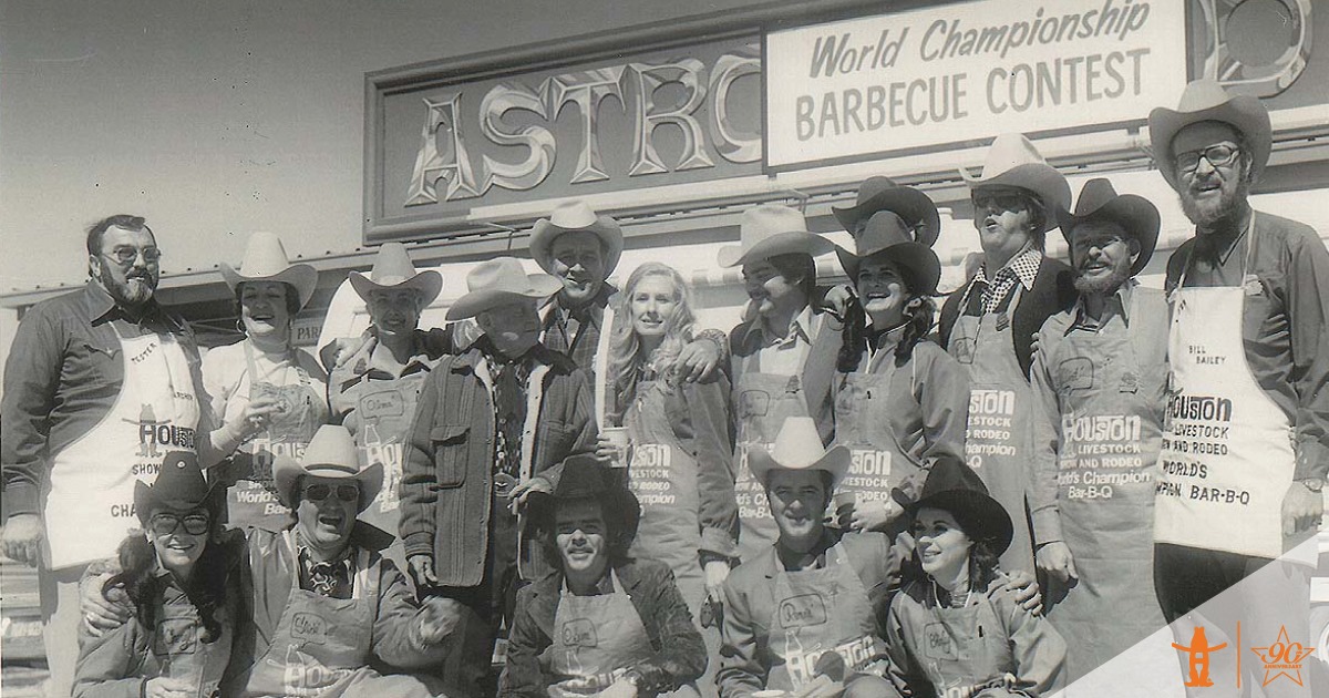 A group of people posing in front of a world's championship bar-b-que contest sign at the Houston Rodeo.